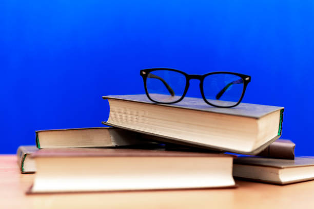 istock Books and eyeglasses on a wooden table, on blue soft background 1803740968