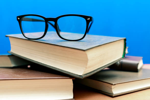 istock Books and eyeglasses on a wooden table, on blue soft background 1803740969