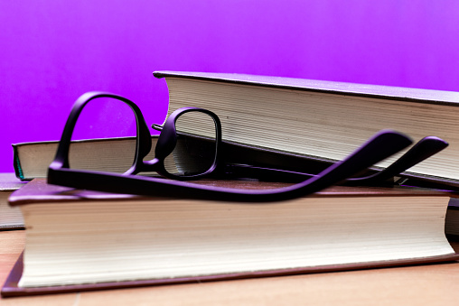 Books and eyeglasses on a wooden table, on purple trendy soft background