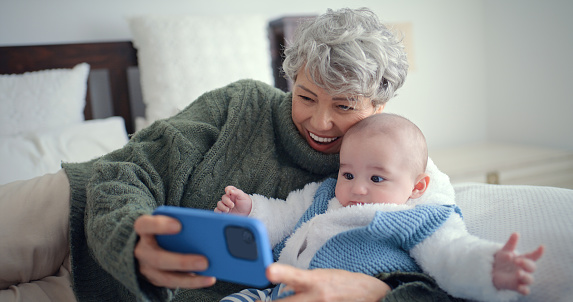 Happy, selfie and grandmother with baby in the living room for bonding and walking together. Smile, love and senior woman in retirement taking a picture with boy child, infant or newborn at home.