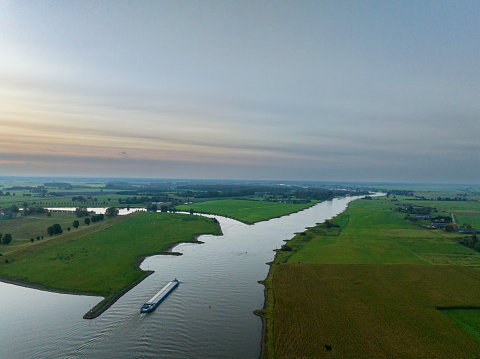 Freight ship barge sailing into the distance on the river IJssel in Overijssel, Netherlands during an autumn sunrise.