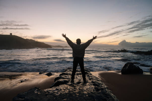 istock Man with arms raised by the sea at dusk 1803753034
