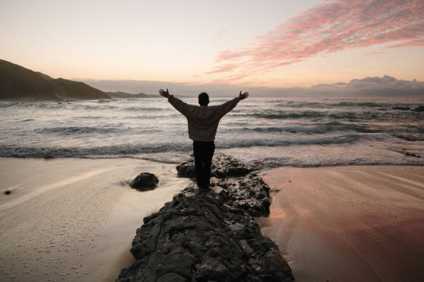 istock Person with arms raised at a beach at sunset 1803754764