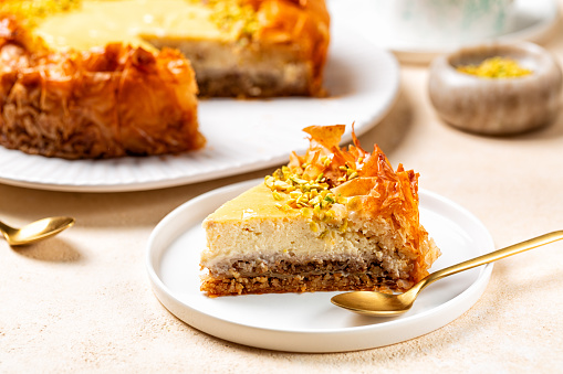A piece of homemade Baklava cheesecake with pistacchio. Light cream cheese filling on top of walnut-filled filo pastry layers soaked in aromatic honey syrup. Sweet pastry, baked dessert.