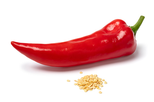 Fresh red pointed bell pepper and a heap of seed in front isolated on white background close up