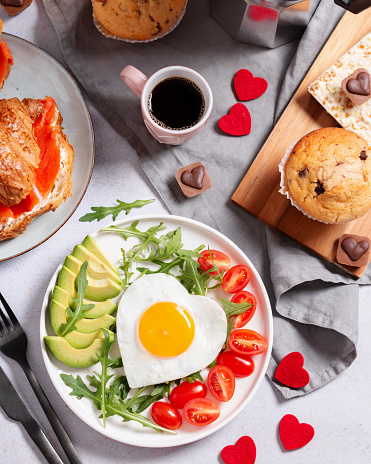 Fried eggs in heart shape, avocado and vegetables, coffee and croissant - surprise breakfast for wife or girlfriend on Valentines Day, Womens Day or Mothers Day. Womens breakfast