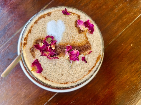 Horizontal flat lay of a homemade chai latte with rose petals and cinnamon sprinkle and white love heart on wood table on saucer with teaspoon in country Australia
