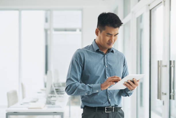 istock Asian man, tablet and research in planning at office for communication, networking or social media. Businessman or employee on technology for online search, strategy or ideas on app at workplace 1803777110