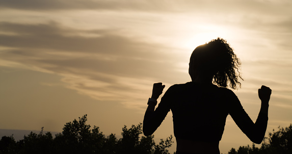 Woman, silhouette and fist pump in celebration for fitness, winning or achievement in nature sunset. Rear view of female person in success or motivation for workout, exercise or outdoor training