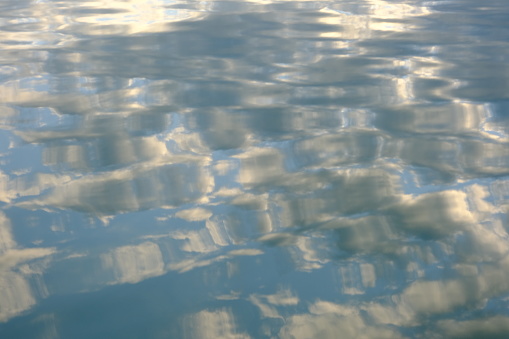 Water of a lake mirrors the sky above, creating a mesmerizing pattern of clouds reflected on the surface, blurring the line between water and air.