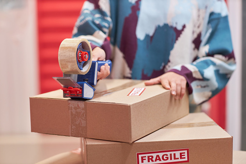 Hands of woman taping boxes with belongings when packing fragile items