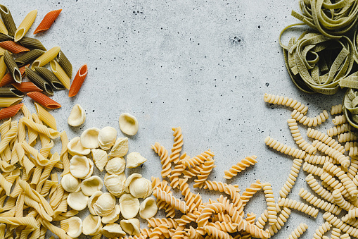 Top view of variety of uncooked pasta on white background. Different types and shapes of dried pasta on kitchen table with copy space.