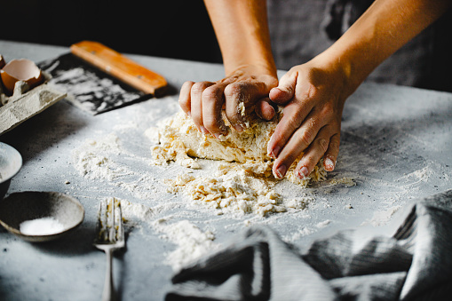 Close-up of hands kneading pasta dough on kitchen counter. Female hands preparing homemade pasta dough.