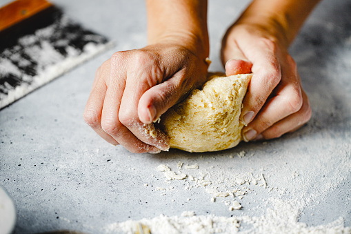 Close-up of woman hands kneading pasta dough. Female preparing dough making homemade pasta in kitchen.