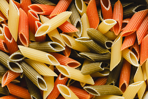 Full frame of multicoloured pasta. Raw uncooked three colored penne pasta.