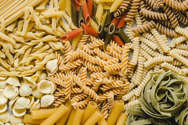 Table top view of variety of uncooked pasta Table top view of variety of uncooked pasta. Full frame of different types of dried pasta on table. spinach pasta stock pictures, royalty-free photos & images
