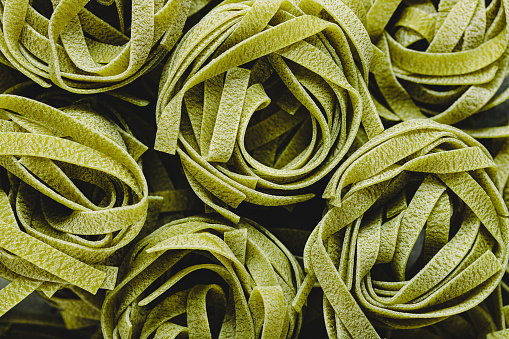 Close-up of raw spinach Fettuccine pasta. Full frame of raw and uncooked green Fettuccine pasta.