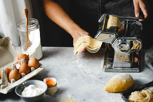 Close-up of female hands making homemade pasta in the kitchen. Woman making homemade pasta at home with a machine.
