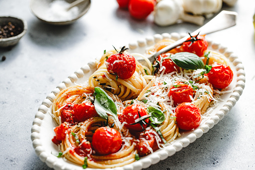 Close-up of freshly prepared tomato basil pasta served in a plate. Homemade spaghetti with tomato and garnished with grated cheese and basil.