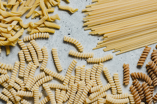 Top view of a variety of types and shapes of Italian pasta on marble background. Different types of dried pasta on white table.