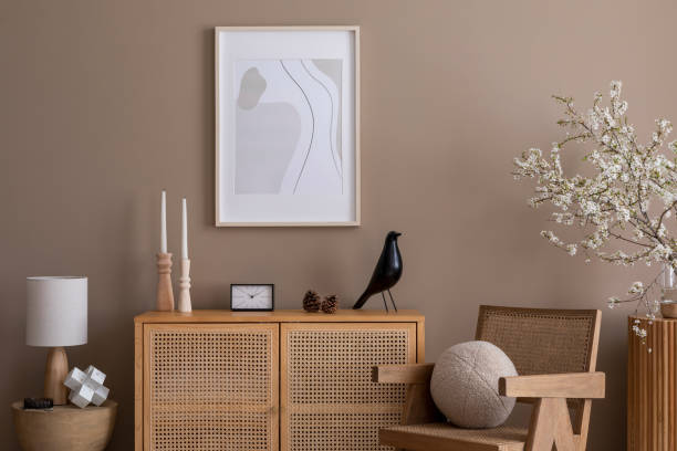 istock Spring composition of cozy living room interior with mock up poster frame, rattan sideboard, wooden armchair, round pillow, sculpture, cherry blossoms and personal accessories. Home decor. Template. 1803828200