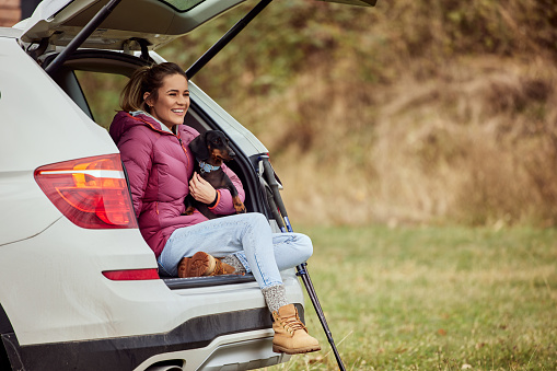 A female dog owner and a dachshund, enjoying nature together, sitting in the car trunk.