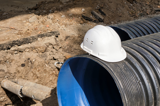 Close-up of a white plastic safety helmet on a black corrugated pipe. The work of public utilities to improve the infrastructure of the metropolis.