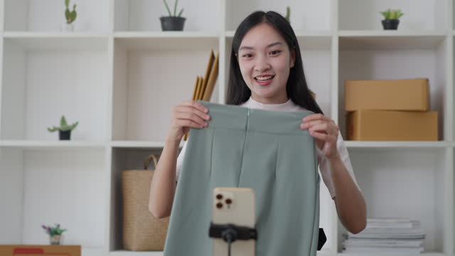 Young Asian woman showing her clothing products to her online customer on her live sell channel