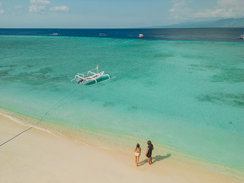 Aerial view of woman and man walking on idyllic tropical beach on Gili Islands during their romantic getaway