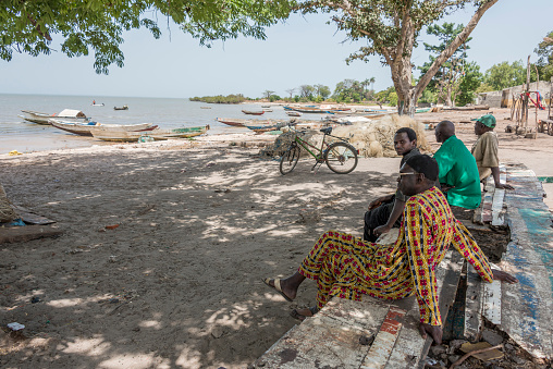 Albreda, Gambia - May 07, 2017: Group of men sitting on the shore next to the Gambia River