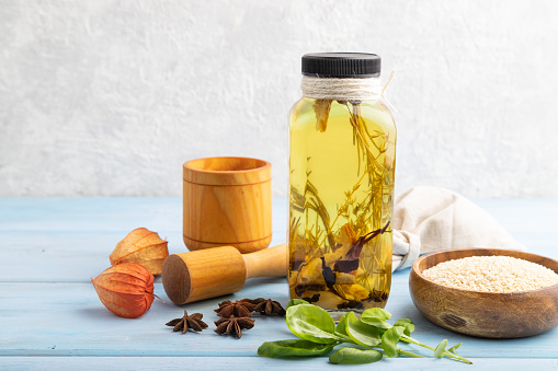 Sunflower oil in a glass jar with various herbs and spices, sesame, rosemary, star anise, basil on a blue wooden background. Side view, copy space.