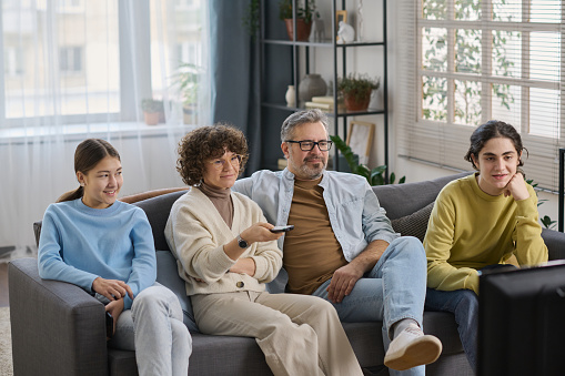 Family of four sitting on sofa and watching TV together at home during their leisure time