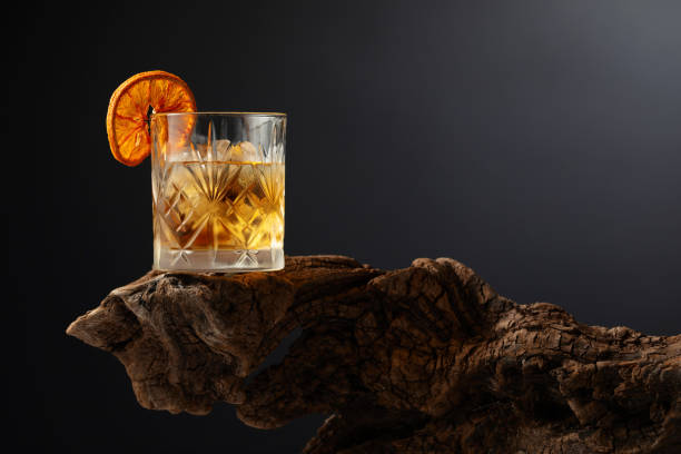 Old fashioned cocktail with ice and dried orange slice on a old snag. stock photo