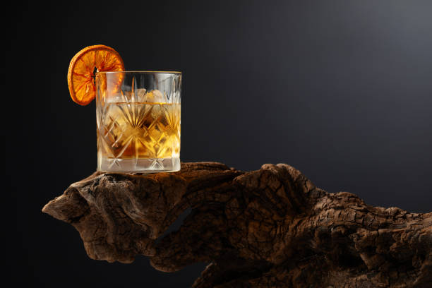 Old fashioned cocktail with ice and dried orange slice on a old snag. Old fashioned cocktail with ice and dried orange slice on a old wooden snag. Black background with copy space. amber black photography stock pictures, royalty-free photos & images