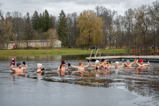 Preili, Latvia - November 18 2023: Group of people ice bathing together in the cold water of a lake in Preili, Latvia. Wim Hof Method, cold therapy, breathing techniques, yoga and meditation