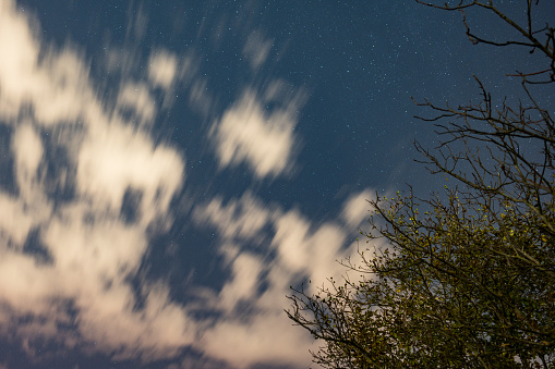 Blurred motion of stars and clouds in a night sky.