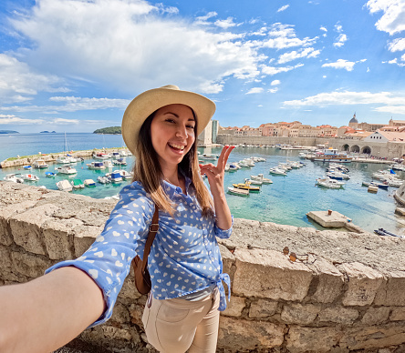 Young woman taking selfies using smart phone in Dubrovnik bay in Croatia.