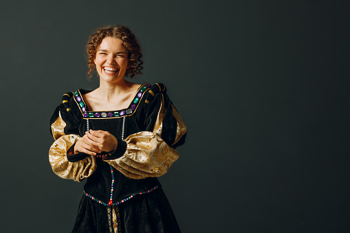 Portrait of a young laughing woman dressed in a medieval dress on dark background