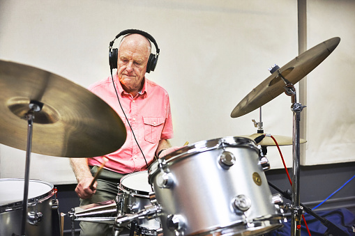 Senior man playing the drums with headphones in a music studio for recording a song, track or album with percussion. Talent, musical career and elderly male person from Australia with an instrument.