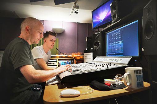 Music, recording studio and a producer team working on a soundboard for art or creative engineering. Technology, audio desk for production and a man technician at a record label with his assistant