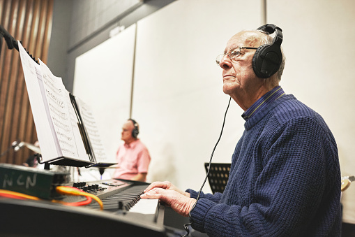 Senior, man and piano player for music, audio or band in orchestra, hall or concert for retirement. Elderly, person and keyboard with headphones, notes and playing for event, musician or serious face