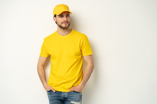 Delivery man in yellow uniform isolated on white background. Professional smiling confident male employee in cap, t-shirt courier dealer. Service concept. Copy space