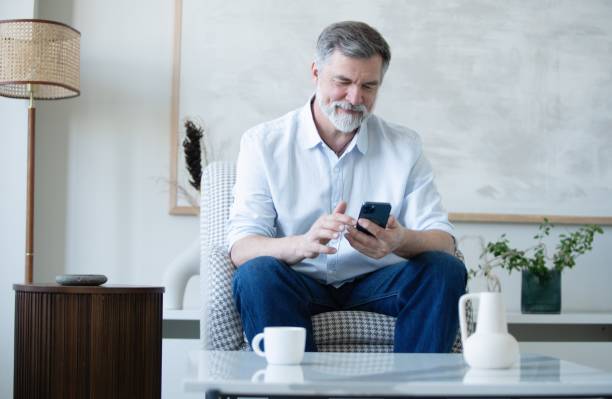 istock Smiling mature freelance businessman using mobile phone checking social media network or message chat sitting on chair at home. 1804029147