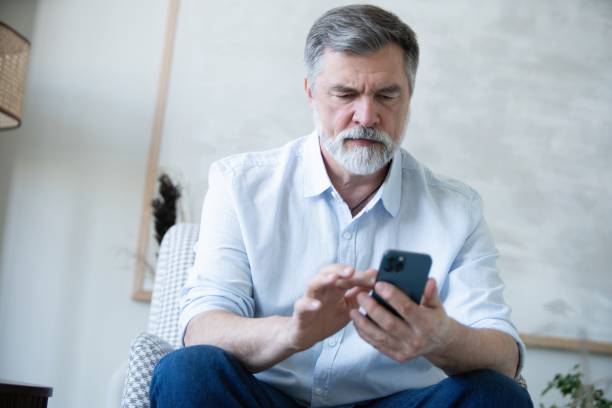 istock Smiling mature freelance businessman using mobile phone checking social media network or message chat sitting on chair at home. 1804029151