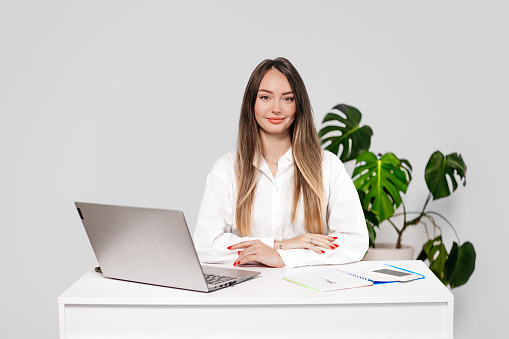 woman psychologist sitting at a table with a laptop smiling at the camera isolated on a white background in the studio