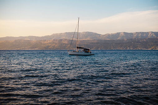Amazing view of white sailboat floating in deep waters of Adriatic sea over big mountains background at sunset. Concept of summer adventure and active vacation in Brac Island.