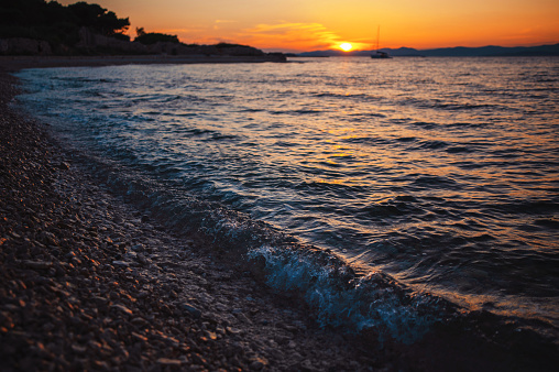 Deserted pebble stone beach during sunset in Croatia. Sea waves hitting coastline in Brac Island. Vacations at seashore of Adriatic sea. Stunning seascape.