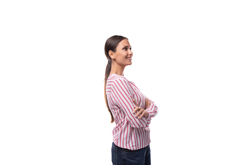 young slender well-groomed brunette leader woman with a ponytail hairstyle dressed in a striped blouse holds her hands on her waist.