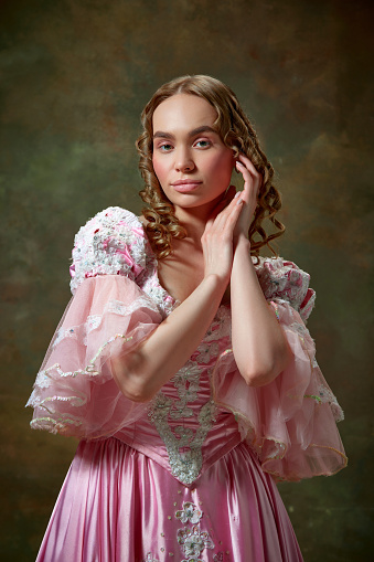 Medieval charming queen. Shot of beautiful woman wearing vintage pink dress and standing with folded hands over vintage texture background. Concept of medieval, beauty, old-fashioned clothes, ad