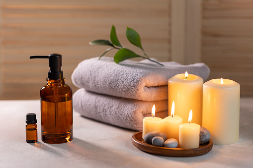 Beauty spa treatment items on white wooden table. Candles, stones, essential oils and towels. Cosy bath.